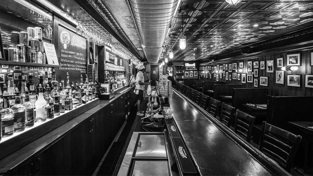Classic black and white bar interior with long counter, menu, and booths.