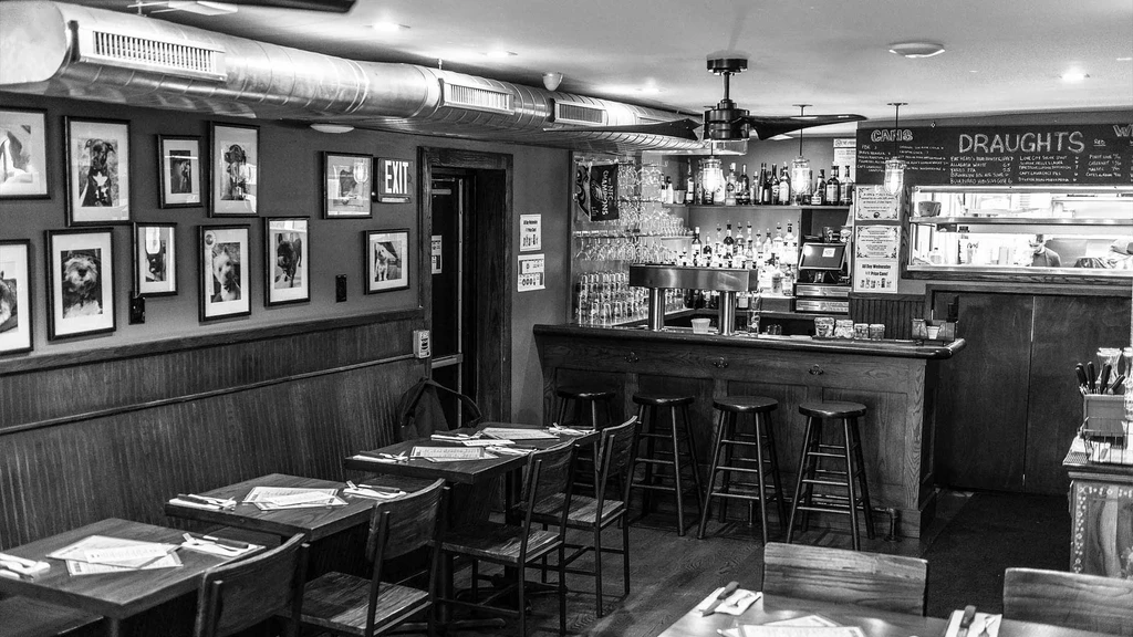 Black and white restaurant interior with bar, dining tables, dog portraits.