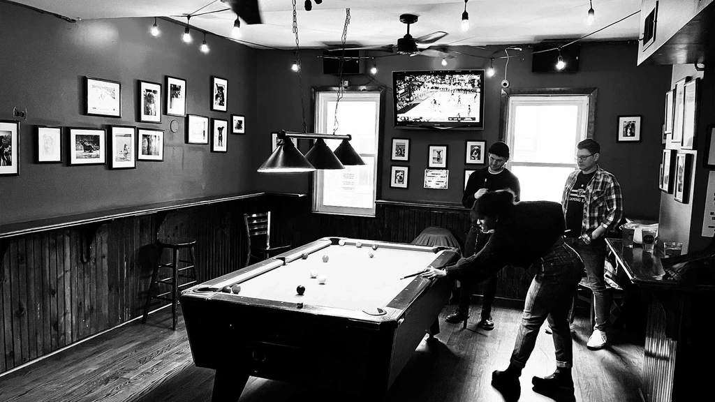 Black and white photo of people playing pool in a bar.