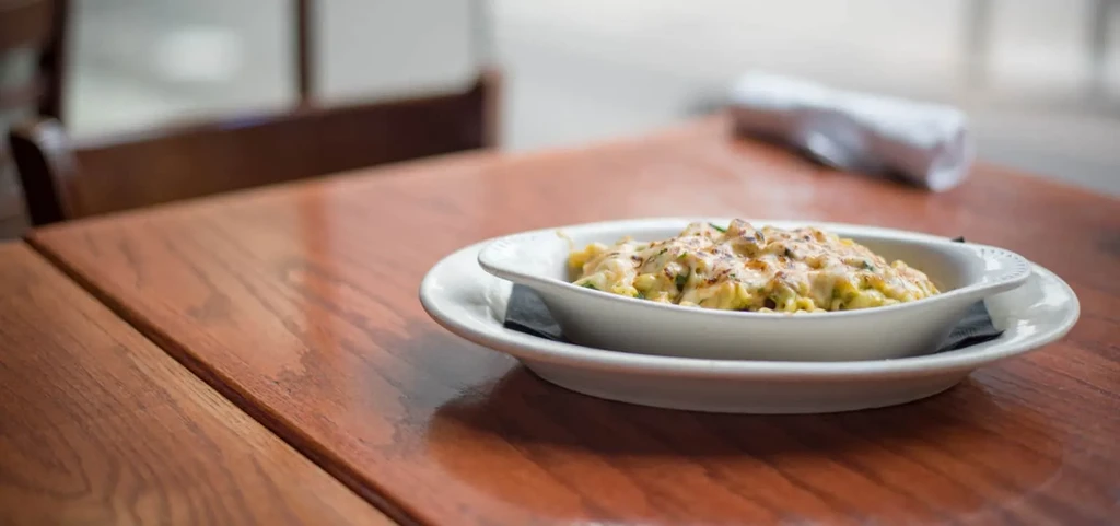 Oval dish of baked pasta with browned cheese on wooden table.