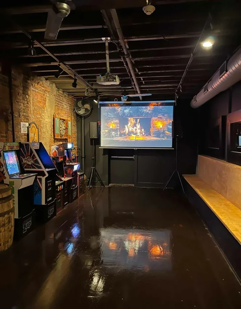Arcade games and projected fireplace in a dimly lit industrial lounge.