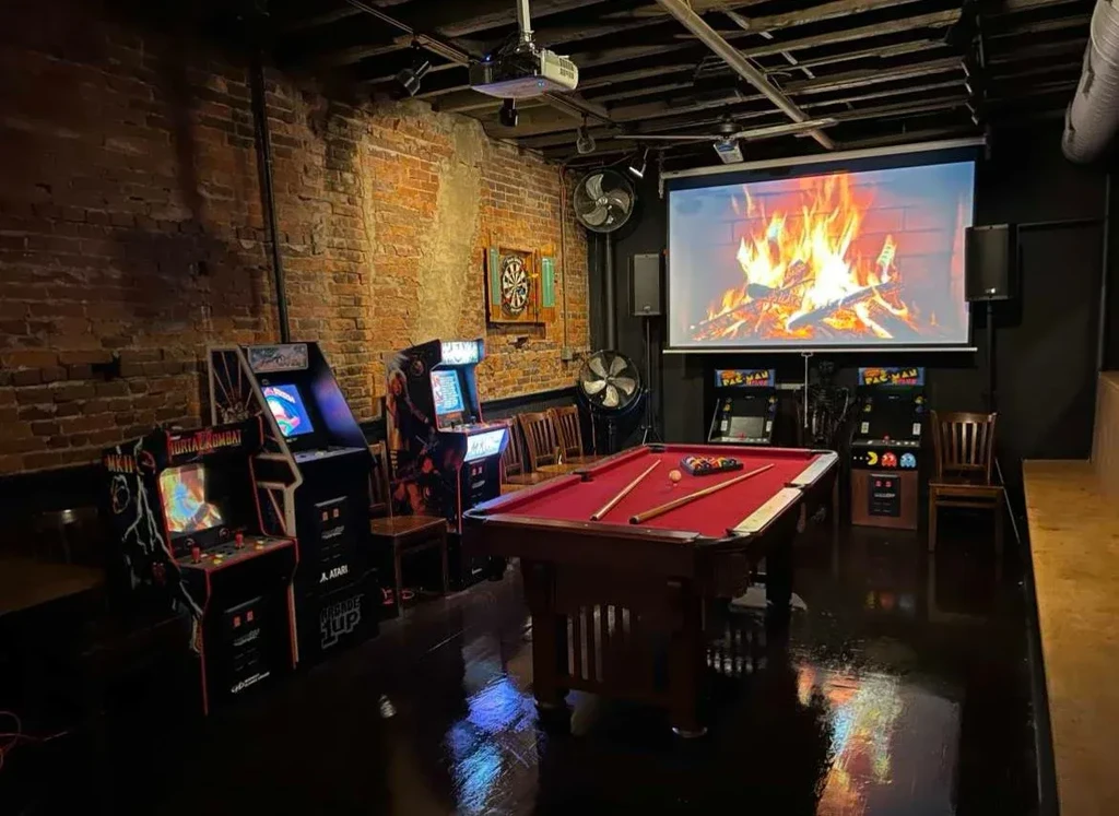 Dimly lit restaurant game room with pool table, arcade, and dartboard.