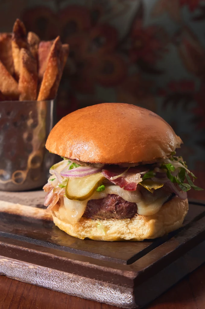 A gourmet burger, fries, and pickles on a rustic wooden board.