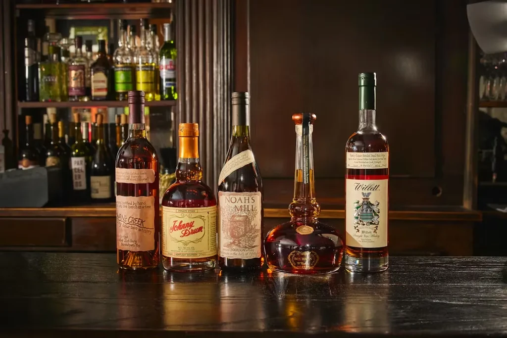 Five whiskey and bourbon bottles on a dark bar counter.