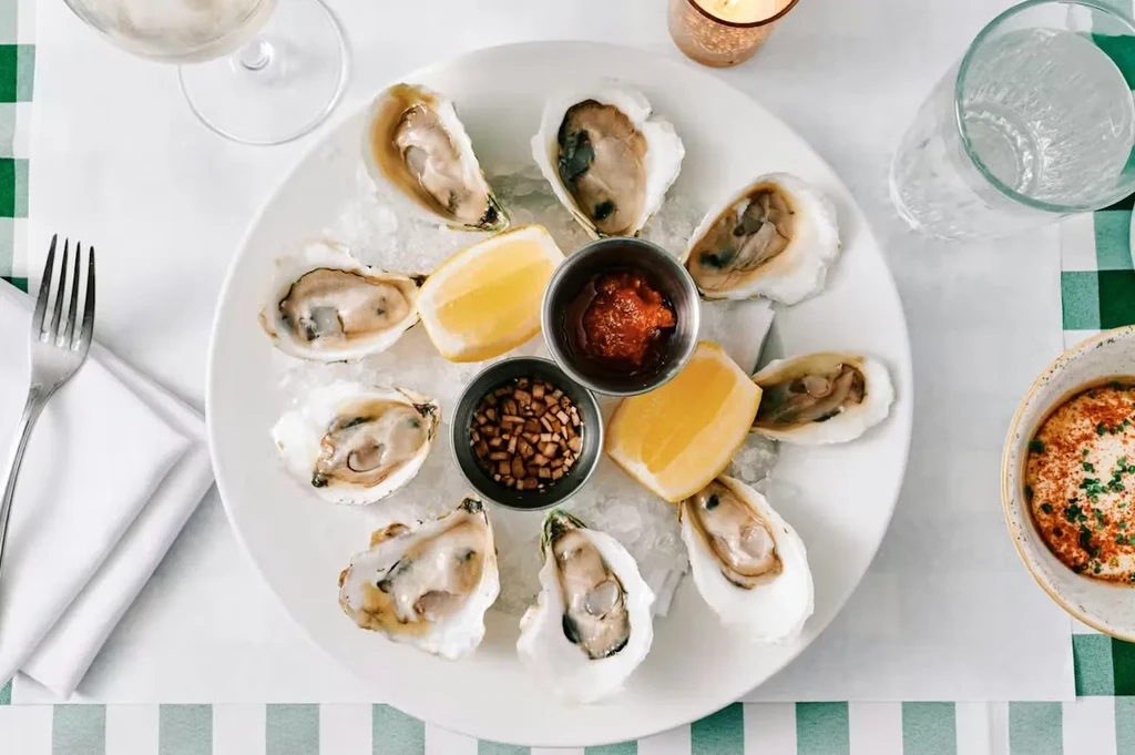 Platter of nine raw oysters on ice with sauces and lemon.