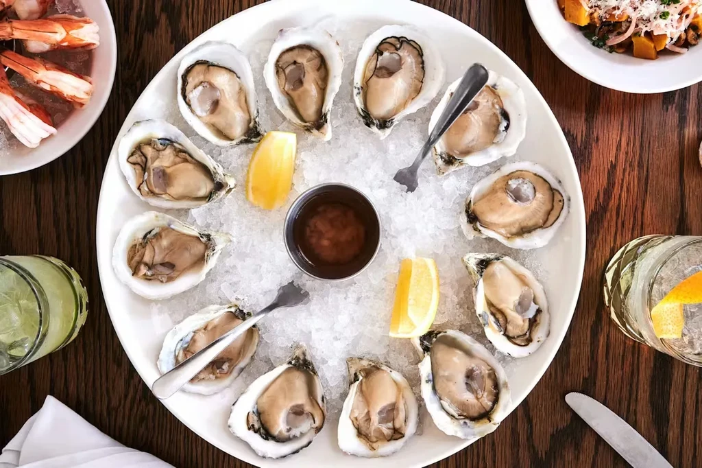 Overhead: Oysters, shrimp, side dish, and cocktails on a dark wooden table.
