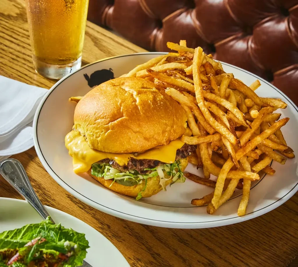 Cheeseburger with fries, beer, and a salad on a wood table.