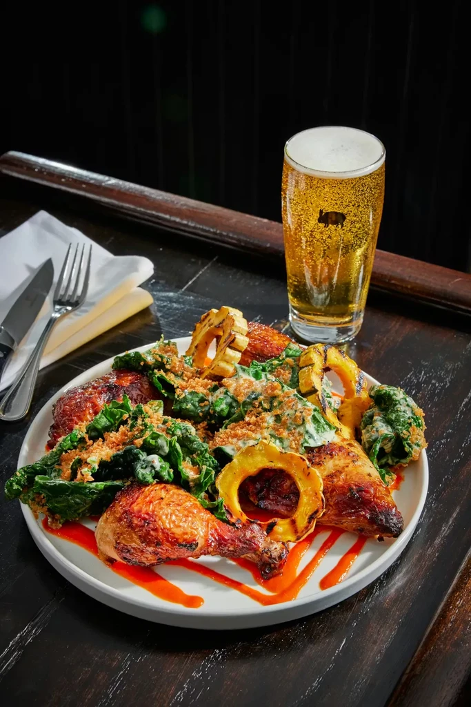 Roasted chicken, vegetables, sauces, and frothy beer with a pig logo.