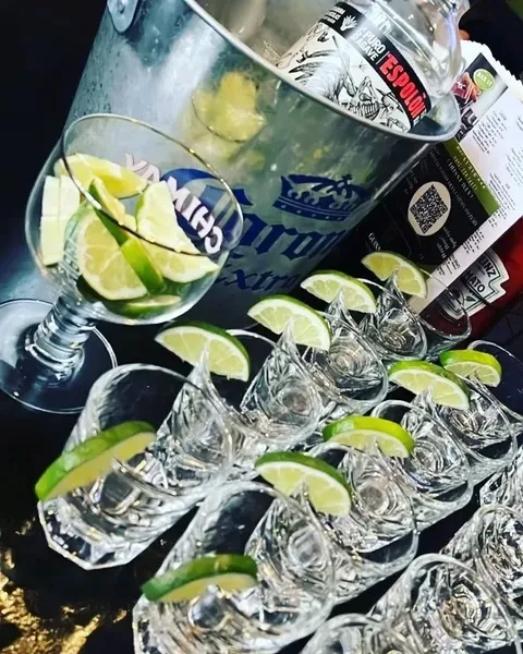 Eleven clear shots with lime wedges, limes, and a tequila ice bucket.