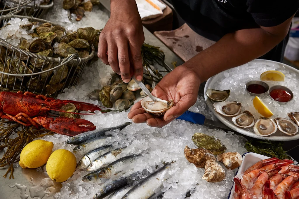 Hands shucking an oyster on a fresh seafood and ice display.
