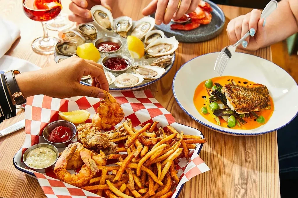 Overhead view of a dining table laden with seafood and reaching hands.
