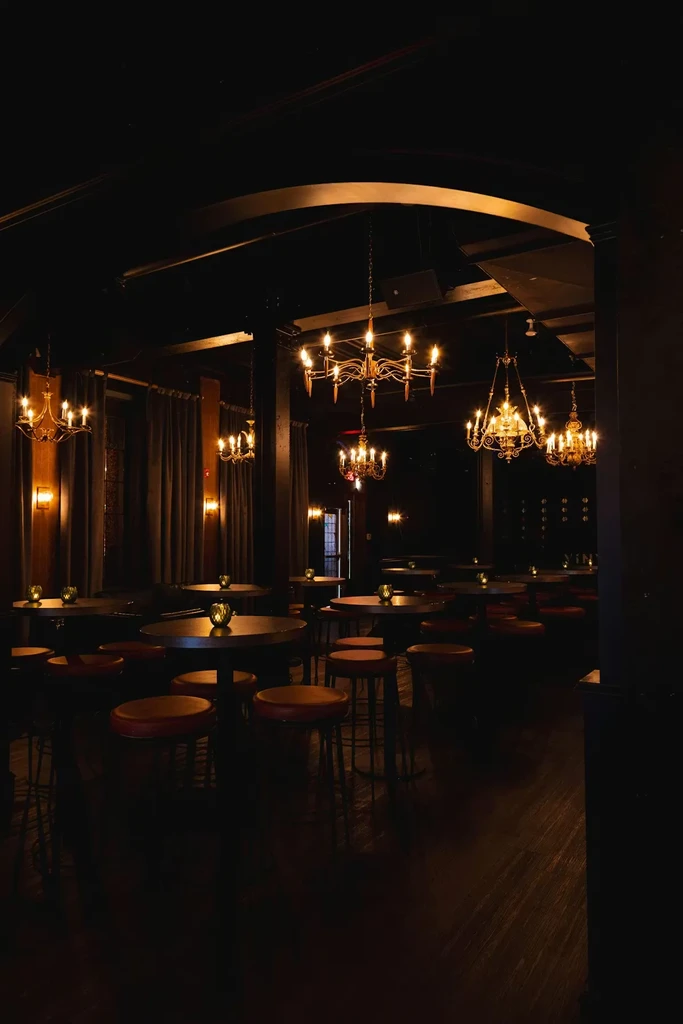 Empty, dimly lit bar interior with high tables, candles, and chandeliers.