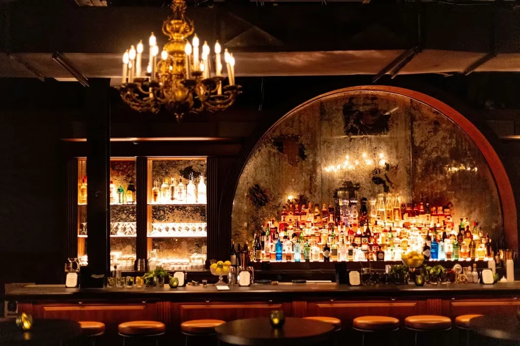 Dimly lit, sophisticated bar with backlit bottles and ornate chandelier.