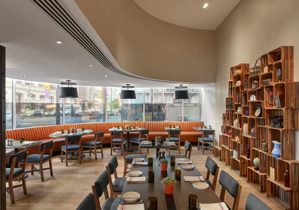 Empty modern restaurant features communal table, orange booths, and crate wall.