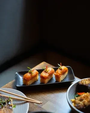 Three garnished fried sushi pieces on a black plate.