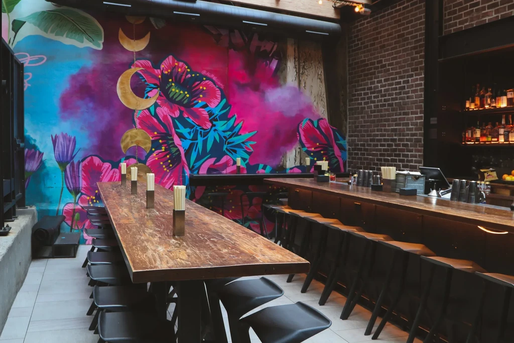 Modern restaurant interior with tropical mural, rustic table, and bar.
