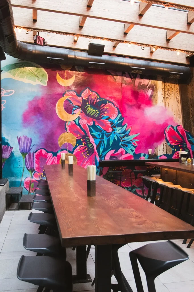 Modern restaurant interior with a colorful floral mural and long communal table.