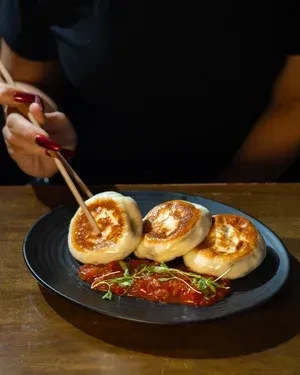 Red-nailed hand uses chopsticks to pick a golden dumpling.