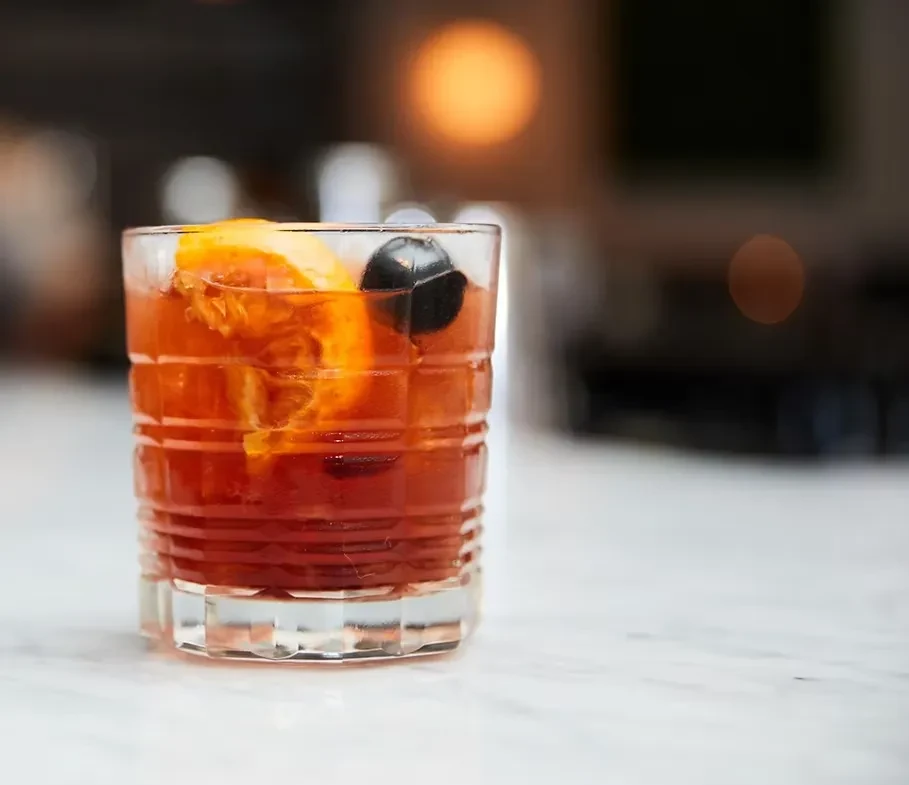 Amber cocktail in a textured rocks glass with orange and dark garnish.