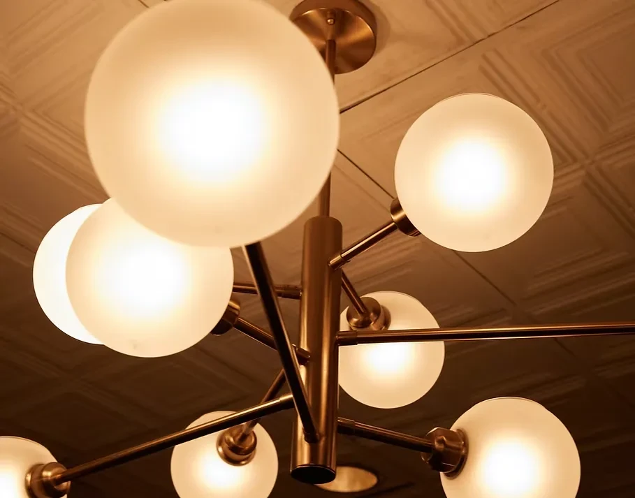 Modern brass chandelier with frosted glass globes hangs from textured ceiling.