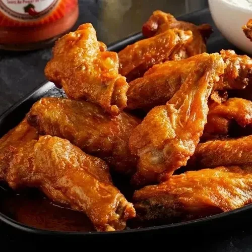 Crispy golden-brown chicken wings with reddish-orange sauce on a dark platter.