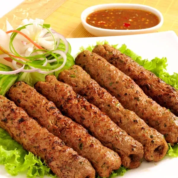 Plate of seven grilled kebabs with fresh vegetables and sauce.