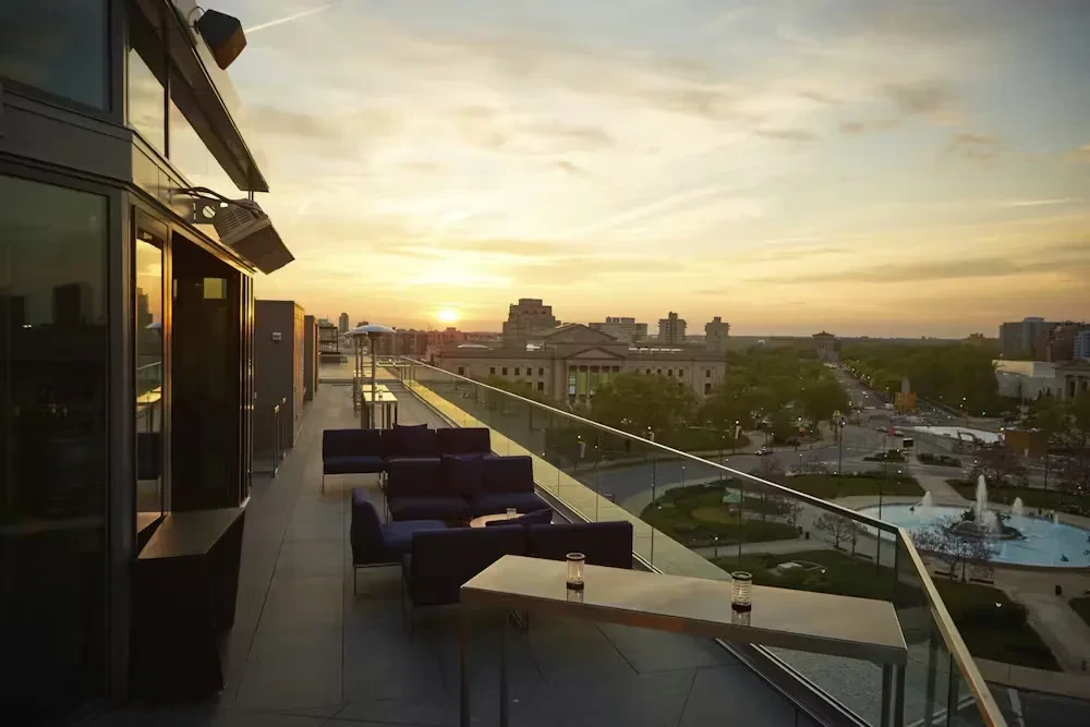 Modern rooftop terrace with seating at sunset, panoramic city view.