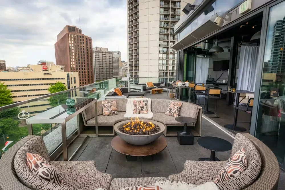 Modern rooftop lounge with curved seating, fire pit, and city skyline.
