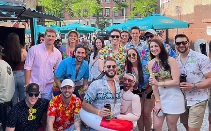 Smiling young adults posing outdoors in Hawaiian shirts with an inflatable doll.