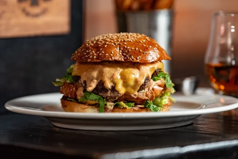 Gourmet burger with melting cheese, creamy sauce, and lettuce on plate.