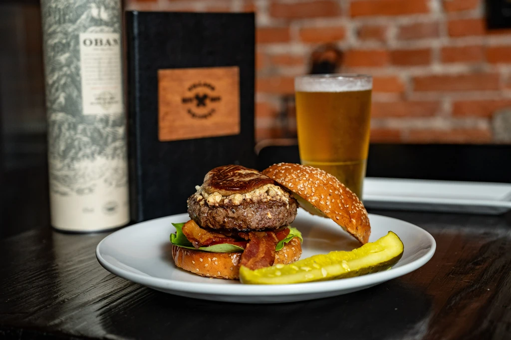 Gourmet burger with cheese and bacon, pickle, and beer.