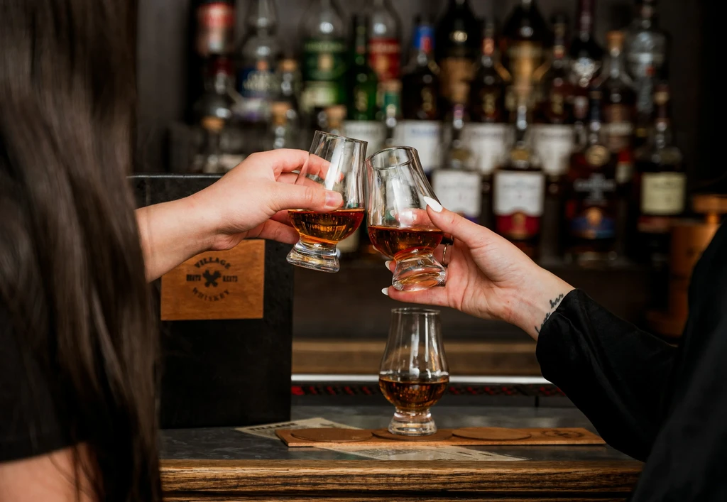Two people clinking Glencairn whiskey glasses at a bar.