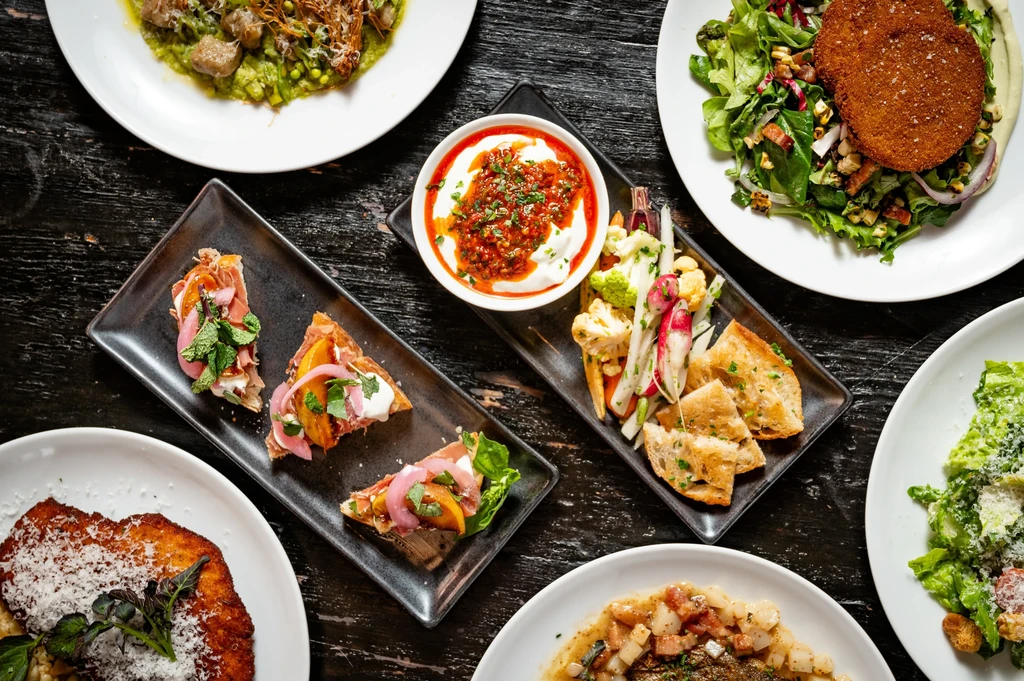 Overhead shot of various artfully plated dishes on a dark wooden table.