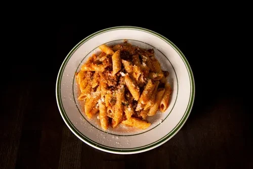 Top-down penne pasta with meat sauce, cheese on a dark background.