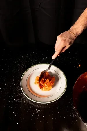 Chef's hands serving rigatoni with red sauce onto a white plate.