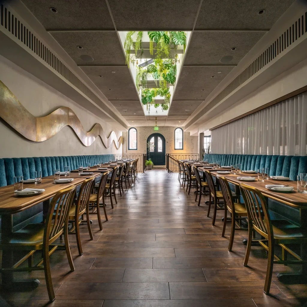Modern restaurant with skylight, hanging plants, teal seating, and wavy art.