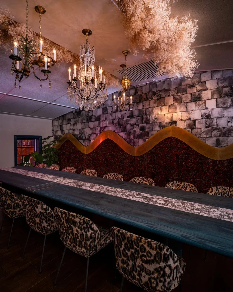 Ornate dining room with long teal table, leopard chairs, red banquette, chandeliers.