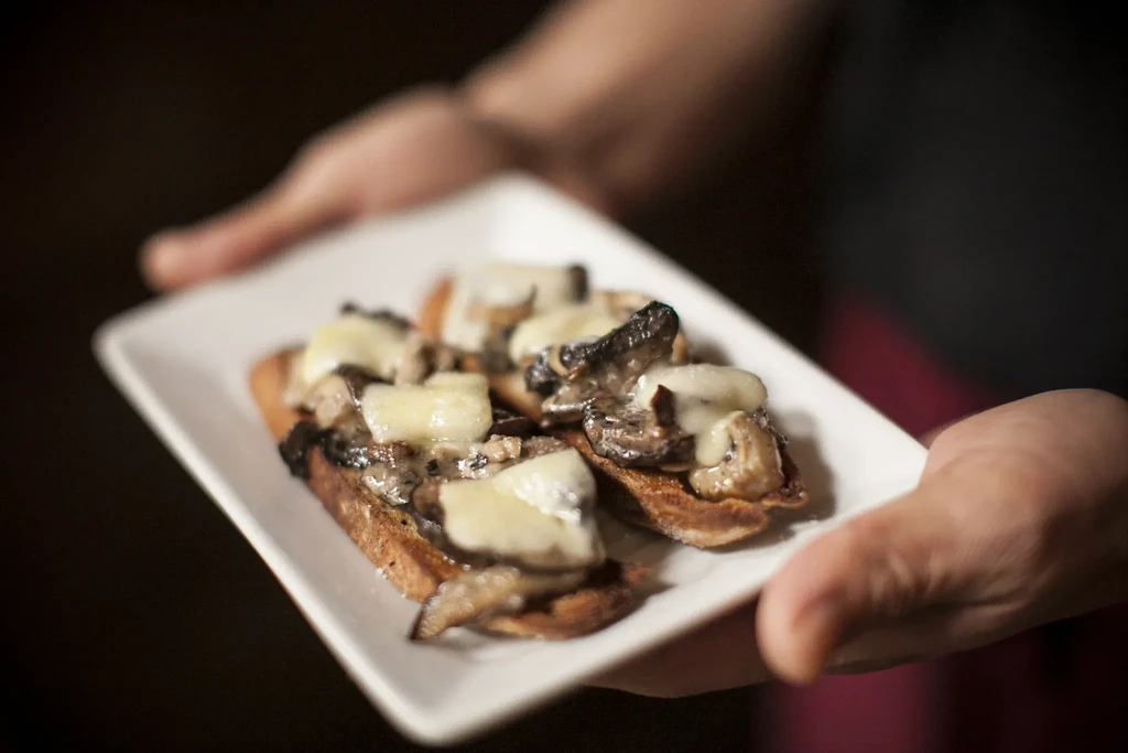 Bruschetta topped with sautéed mushrooms and melted cheese on a white plate.