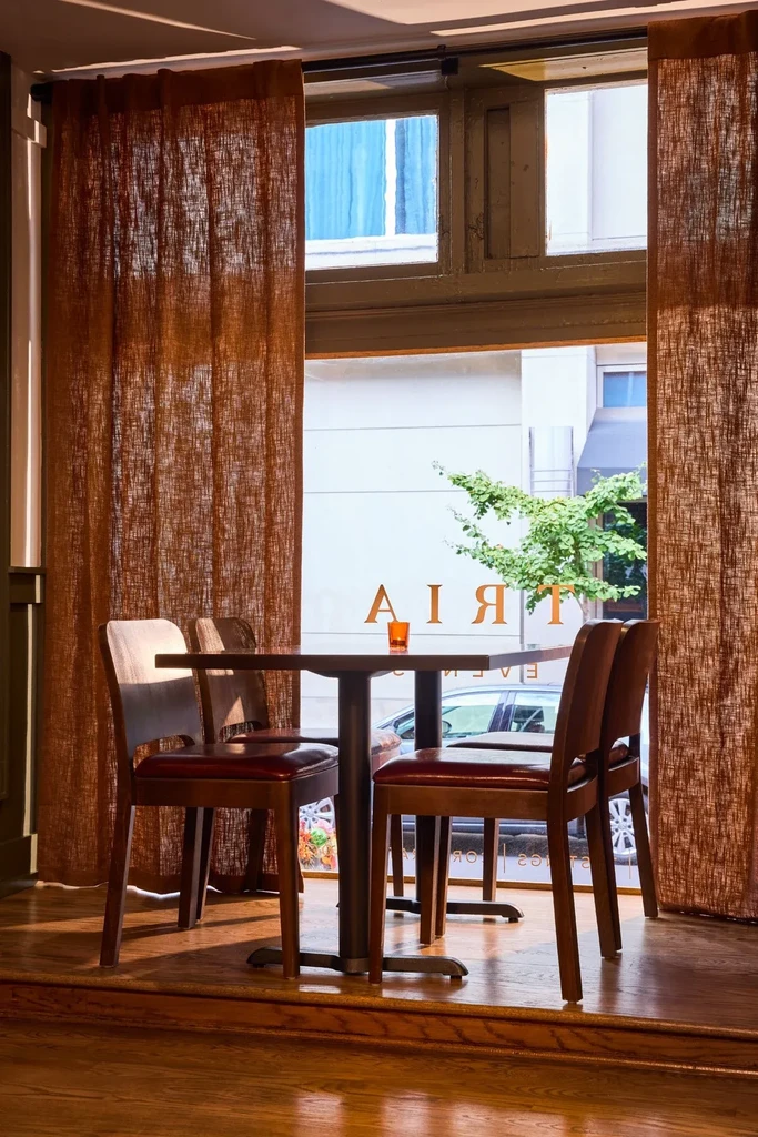 Sunlit cafe corner with table, chairs, and urban window view.