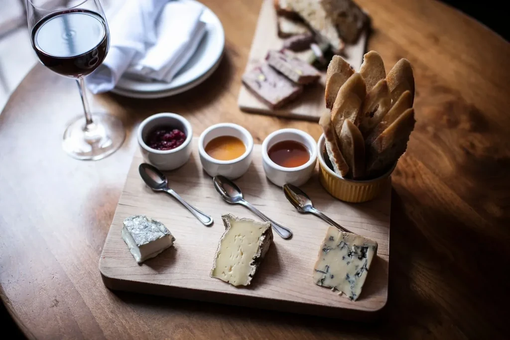 Cheese board with three cheeses, jams, bread, and red wine.