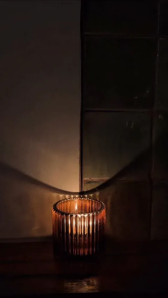 Candle in amber ribbed glass holder glows on dark surface.