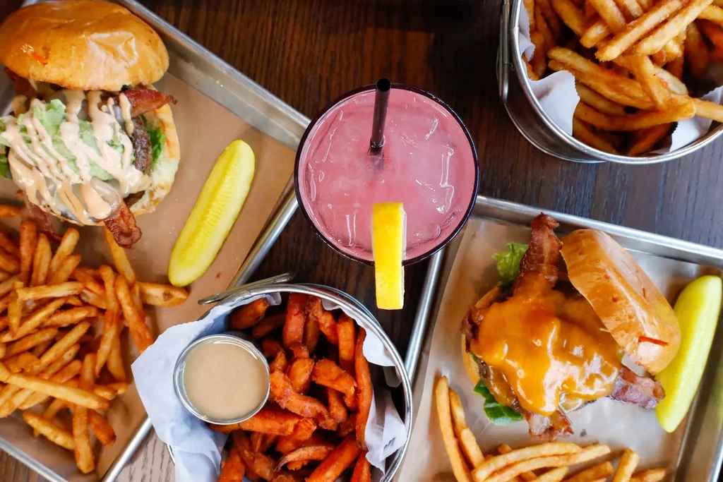 Overhead: two burgers, various fries, and a pink drink.