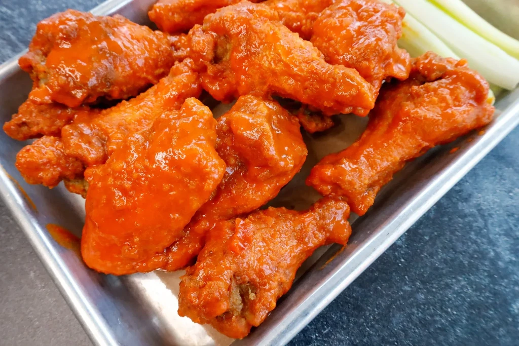 Close-up of saucy buffalo wings in a metal tray with celery.