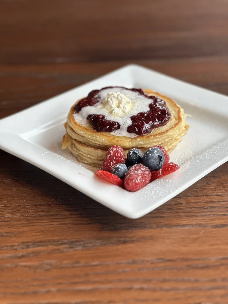 Stack of pancakes with berry compote, fresh berries, and powdered sugar.