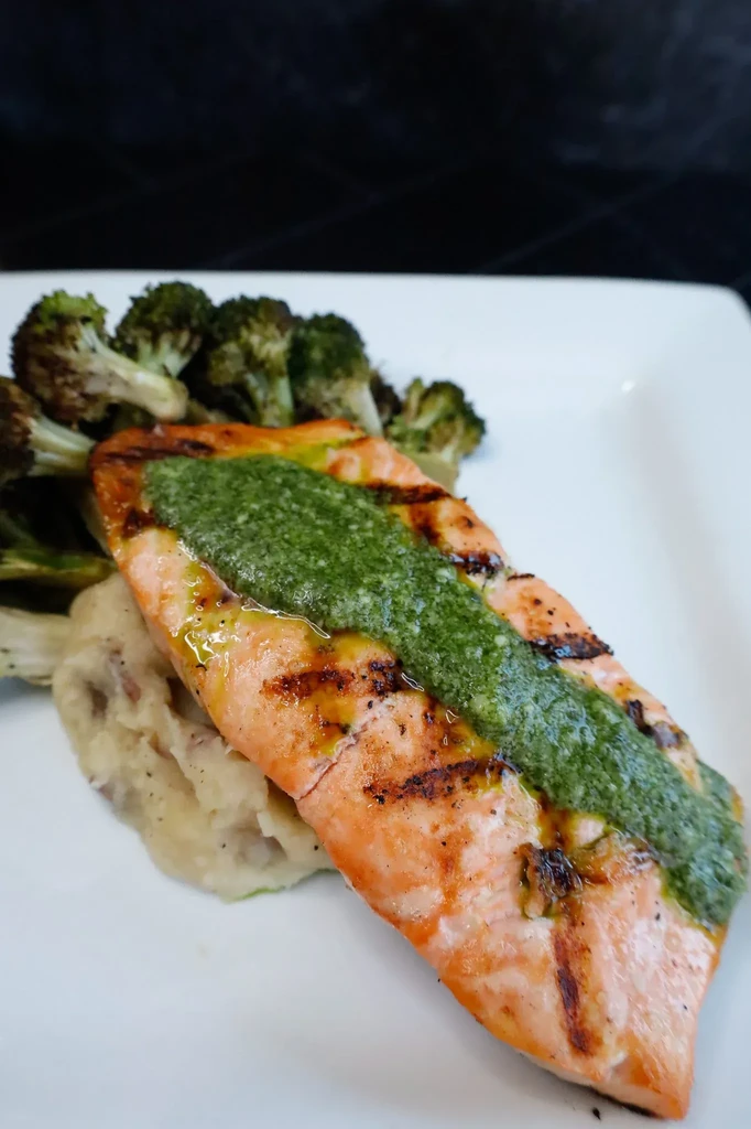 Plated grilled salmon with green sauce, mashed potatoes, and broccoli.