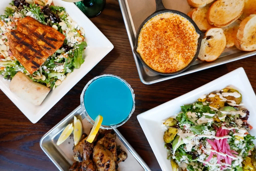 Overhead: Table with salmon, baked dip, blue drink, grilled chicken, brussels sprouts.