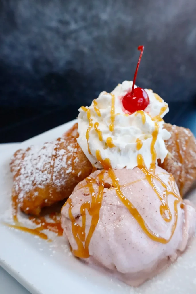 Dessert with golden fried dough, pink ice cream, whipped cream, and cherry.