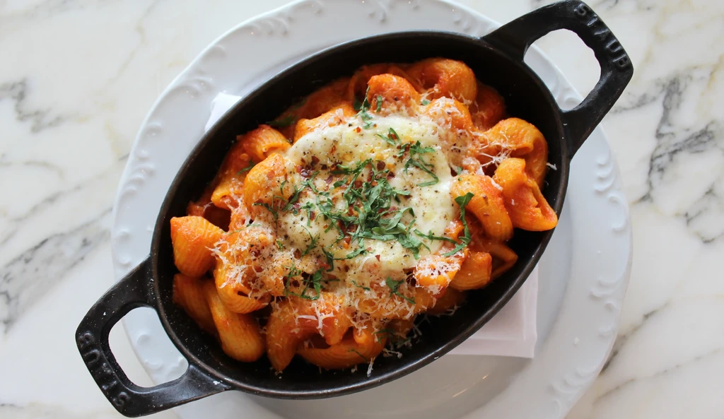 Cast iron pan with pasta shells, red sauce, melted cheese, herbs.