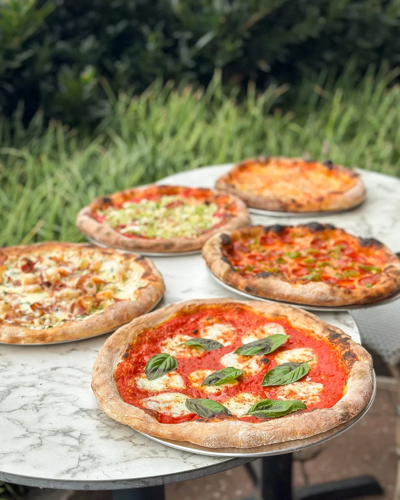 Five individual, freshly baked pizzas on an outdoor marble table.