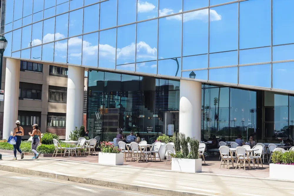 Modern restaurant with reflective facade, people dining on a sunny patio.